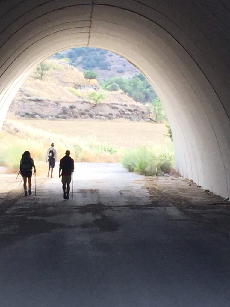 Three figures emerging from a tunnel into hilly terrain