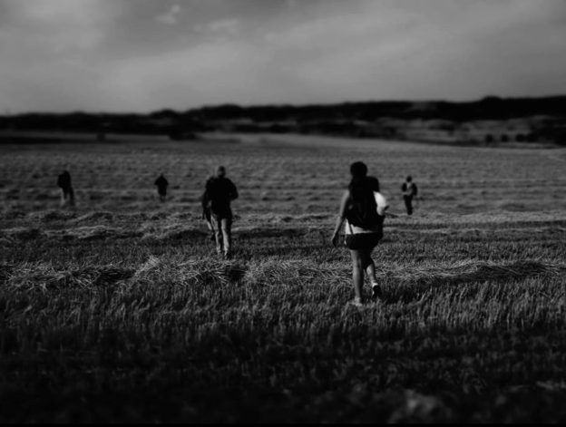 black and white photo of pilgrims walking across grassy field.