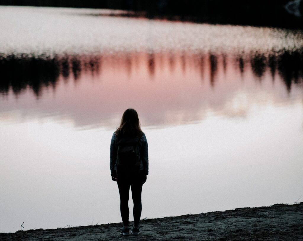 Silhouette of girl looking at lake at twilight