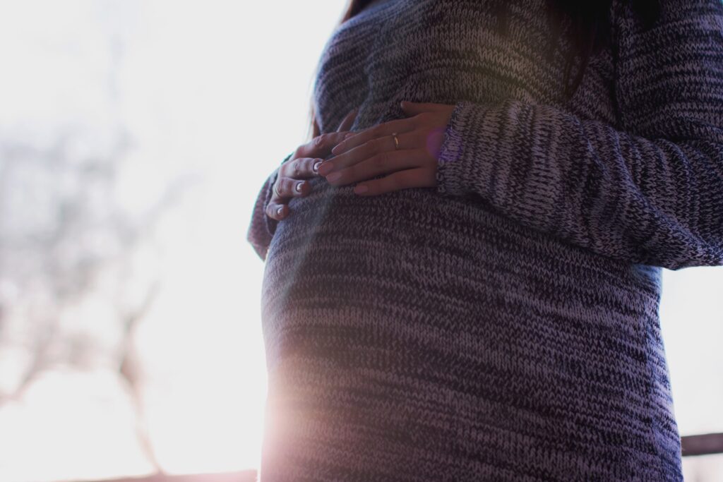 A pregnant person wearing a blue striped sweater rests her hands on her belly